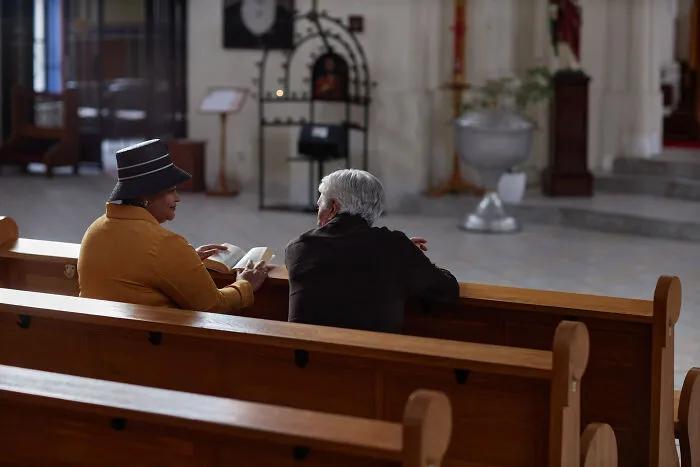 Two older women sit on a church pew reading, reflecting on sobering stories that impact lives.