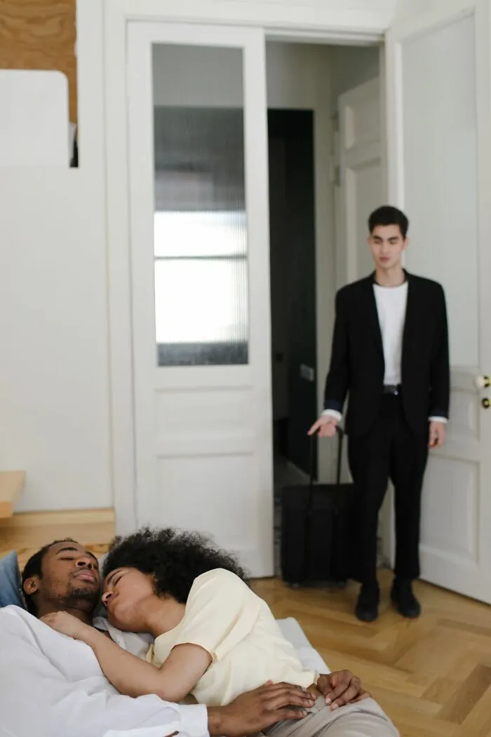 Man arriving with luggage while couple embraces on bed, historic jerk moment scene