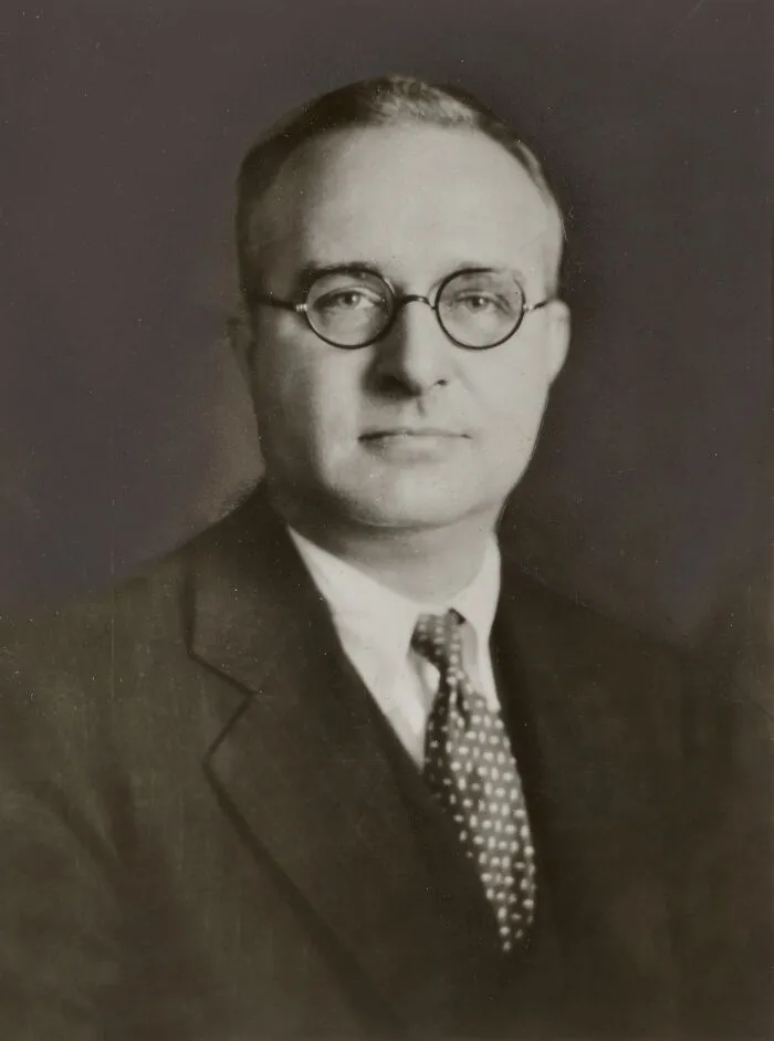 Black and white photo of a man in glasses and suit from history