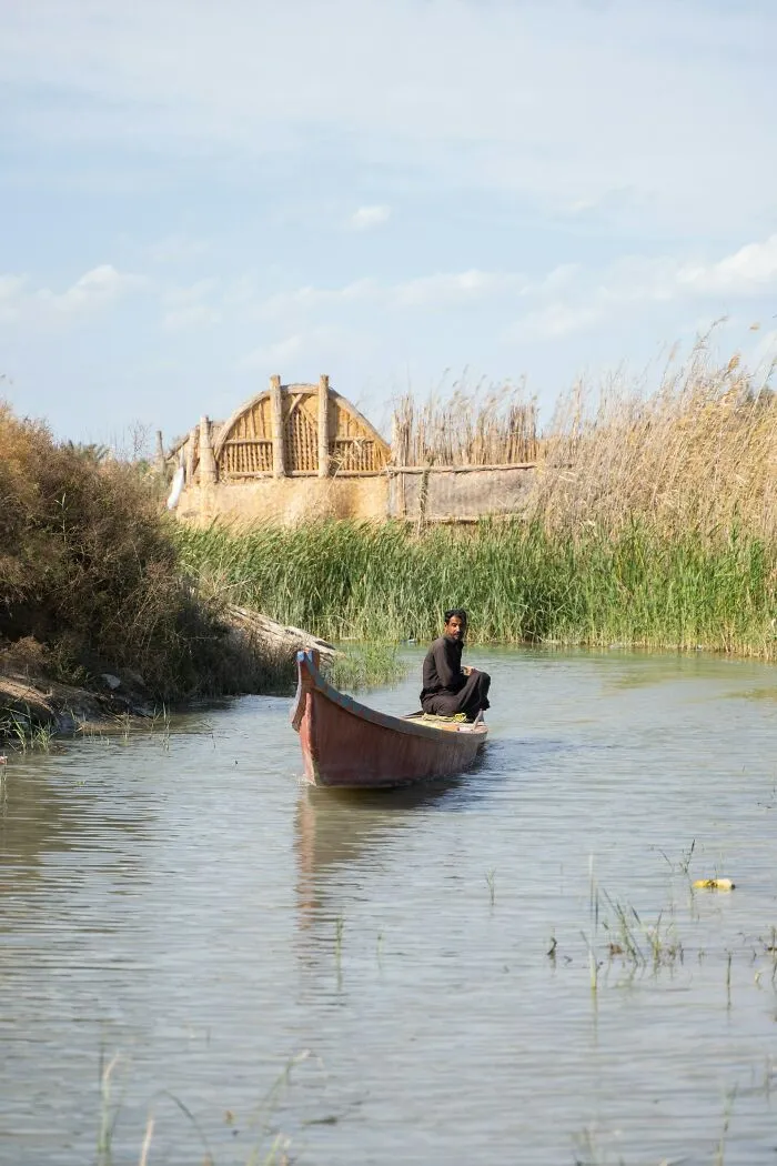 Man paddling a boat on a narrow river surrounded by reeds