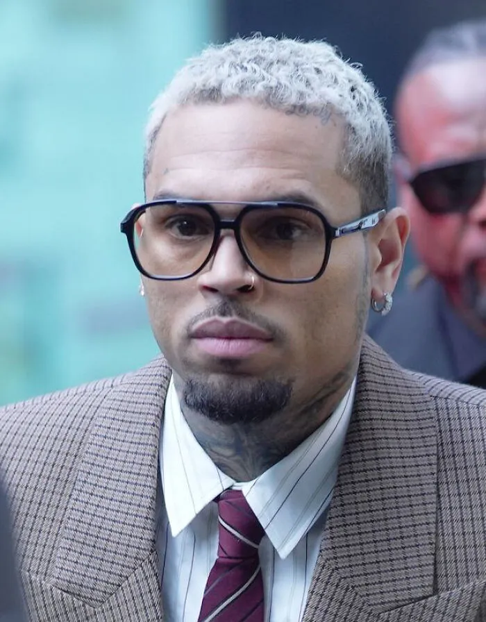 Chris Brown wearing glasses and a striped tie, representing stars with public career challenges.