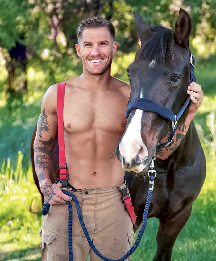 Smiling firefighter with tattoos and suspenders holding black horse with blue halter