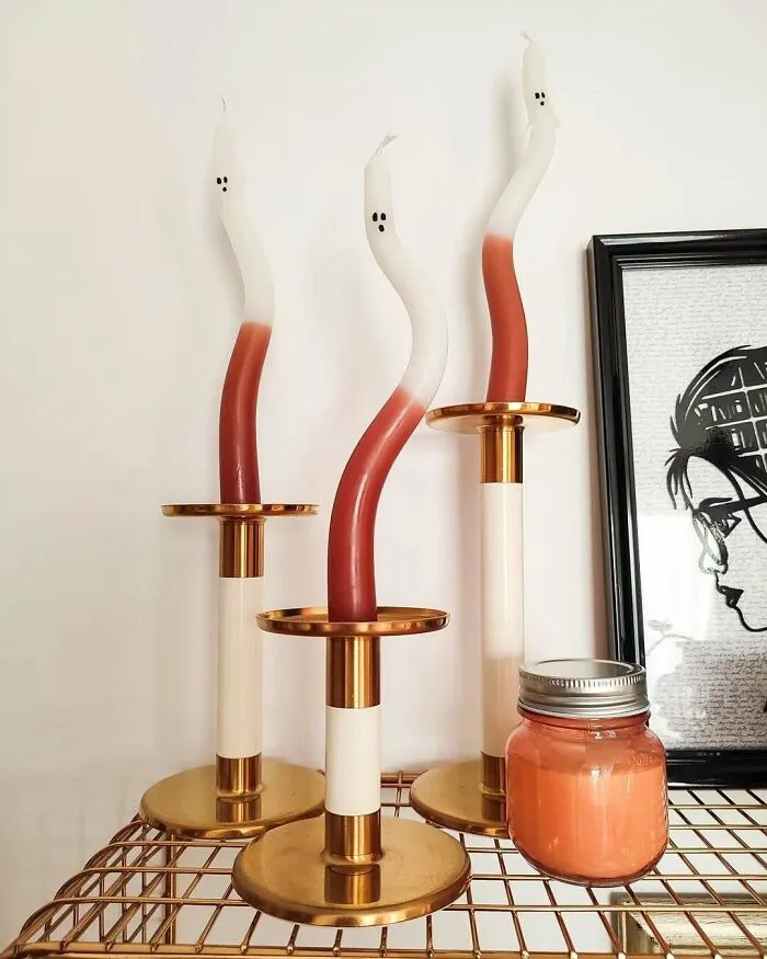 Ghost-shaped candles in brass holders set on a table as Halloween home decor.