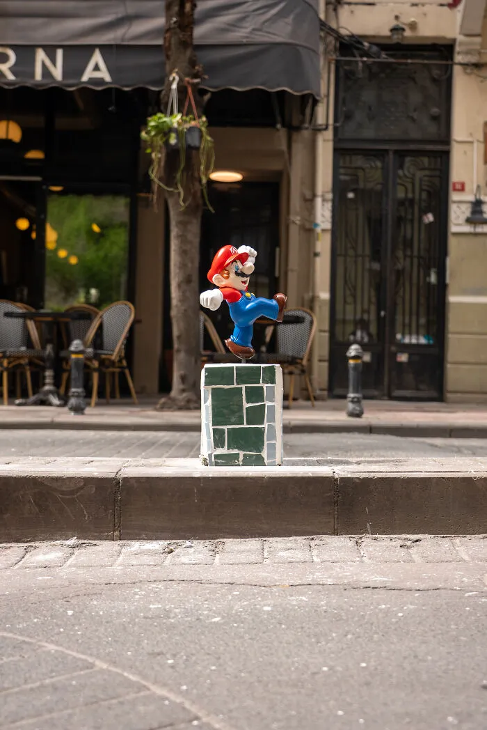 A Mario figurine atop a decorative block on city streets outside a restaurant storefront