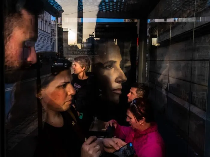 Reflections of people in a dark glass window with a large face poster and urban background
