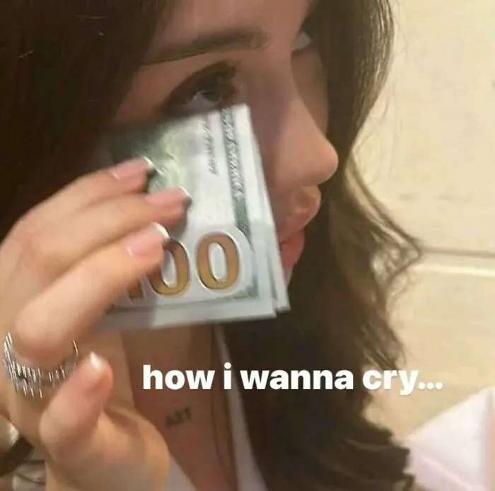 A woman wiping her tears with a stack of hundred-dollar bills in a meme about crying over inconveniences.