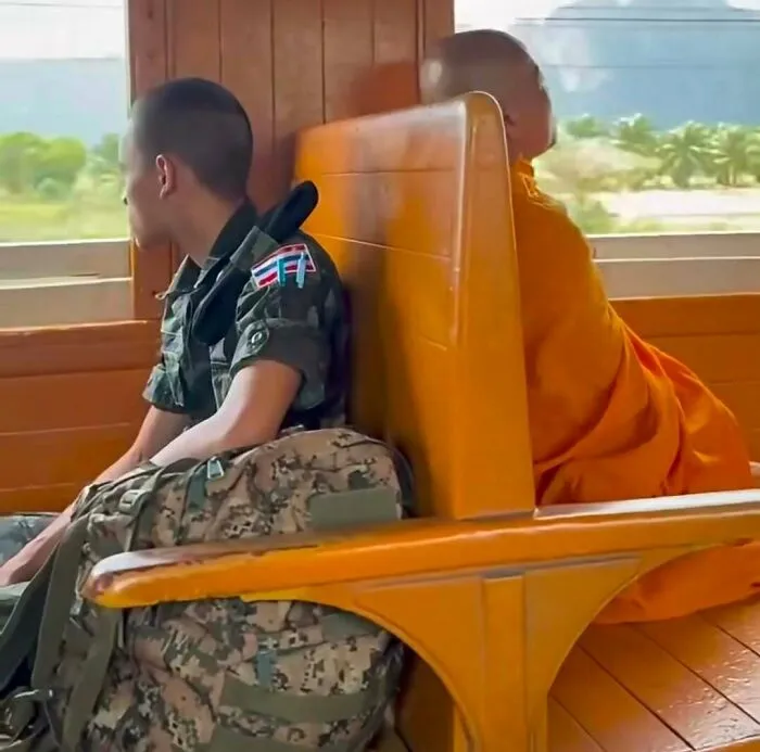 Out-of-context pics of a soldier and a Buddhist monk sitting back to back on a wooden train seat