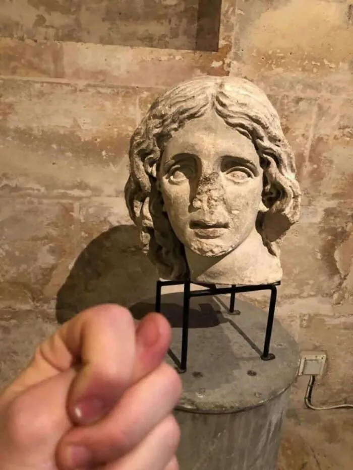Out-of-context pics of a hand pretending to steal the nose off an ancient stone head statue.