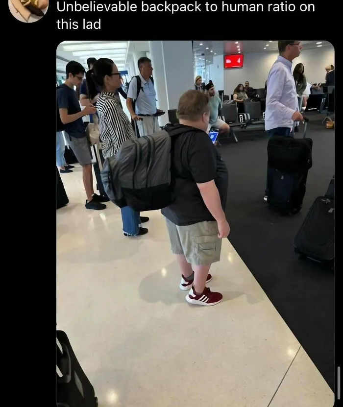 An out-of-context pic of a person standing at an airport wearing a huge backpack that is almost as big as them.