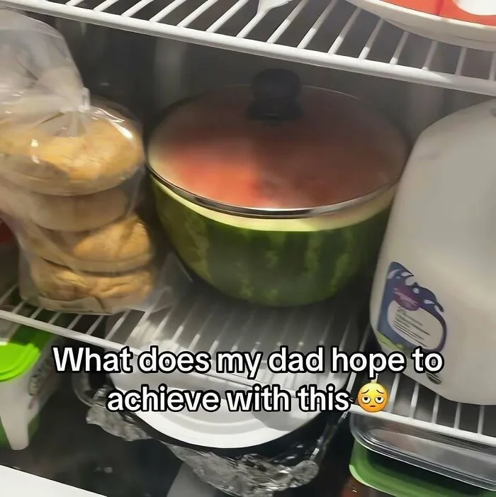 An out-of-context pic showing a cut watermelon covered with a pot lid stored inside a crowded refrigerator.
