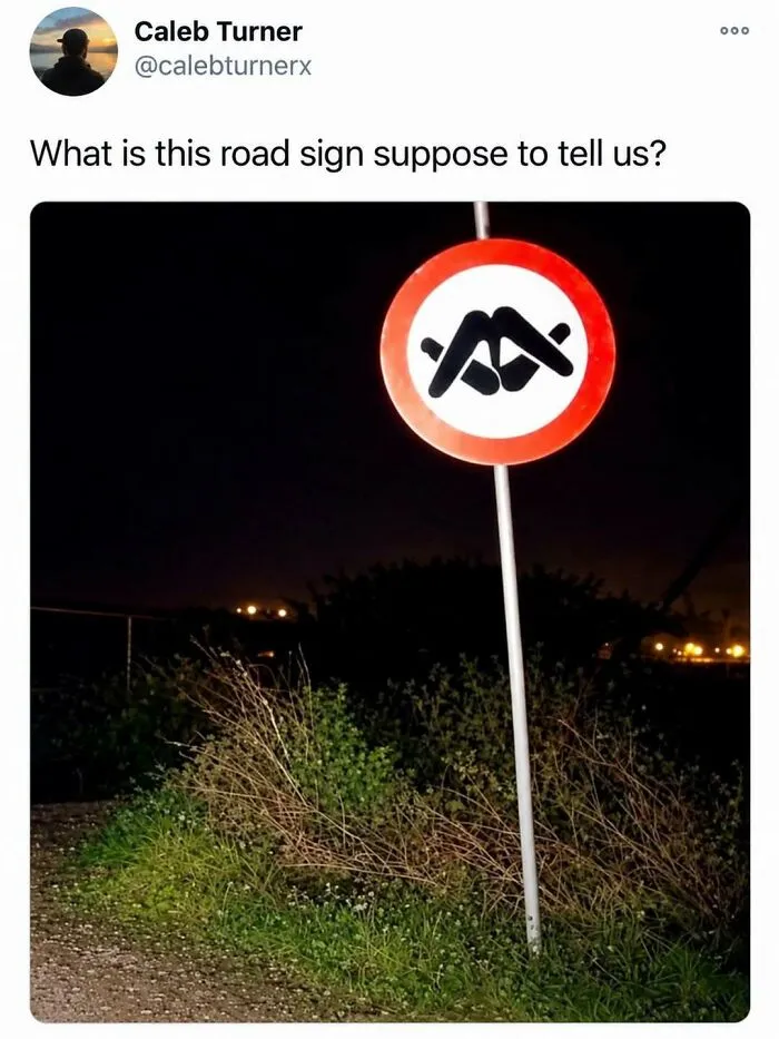 An entertaining post showing a confusing circular road sign at night with abstract black symbols.