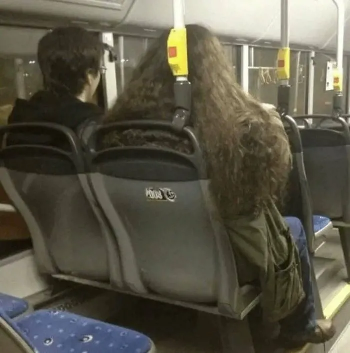 An amusing post showing a person with long hair sitting on a bus seat next to another passenger.