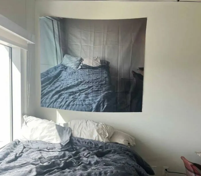 A wall tapestry printed with a photo of a bed hanging directly above a real bed in an amusing post