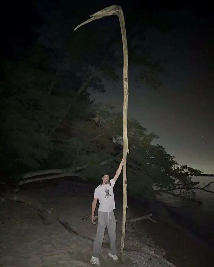 A man holding a giant scythe-shaped stick outdoors showcased in amusing posts