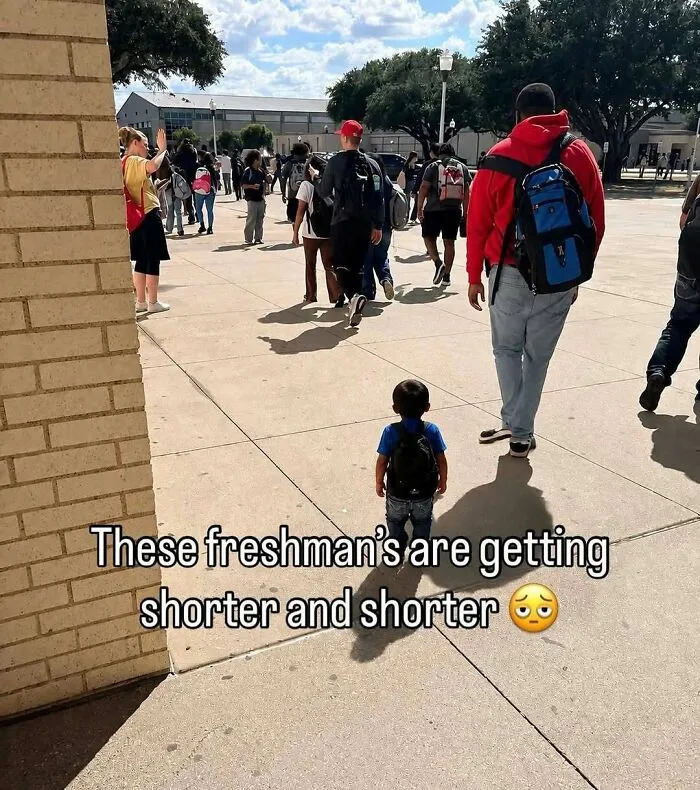 A toddler wearing a backpack walks among older students on a school walkway in hilarious pics.