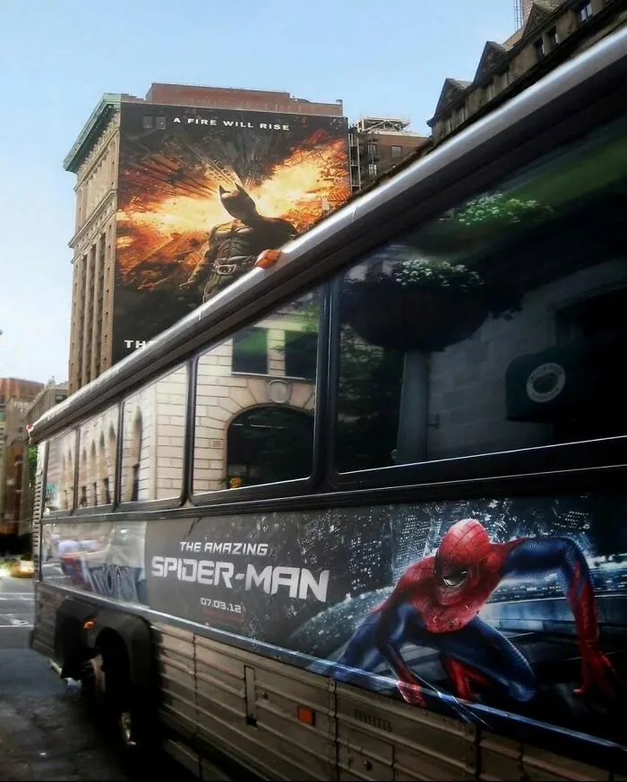 A city street with a Spider-Man bus ad passing under a Batman billboard in hilarious pics.