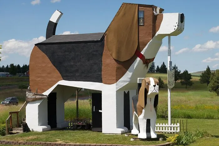 An example of architecture with bizarre shapes featuring a giant dog-shaped house in a grassy field.