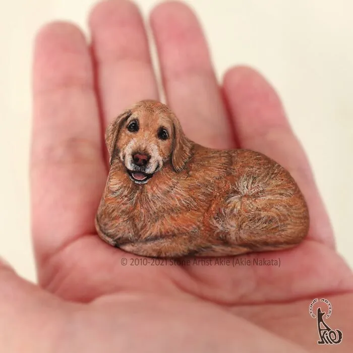 Stone art of a smiling golden retriever dog held in a palm