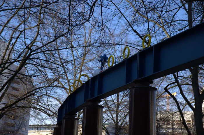 Sonic the Hedgehog figure with gold rings on a blue metal beam in a city park