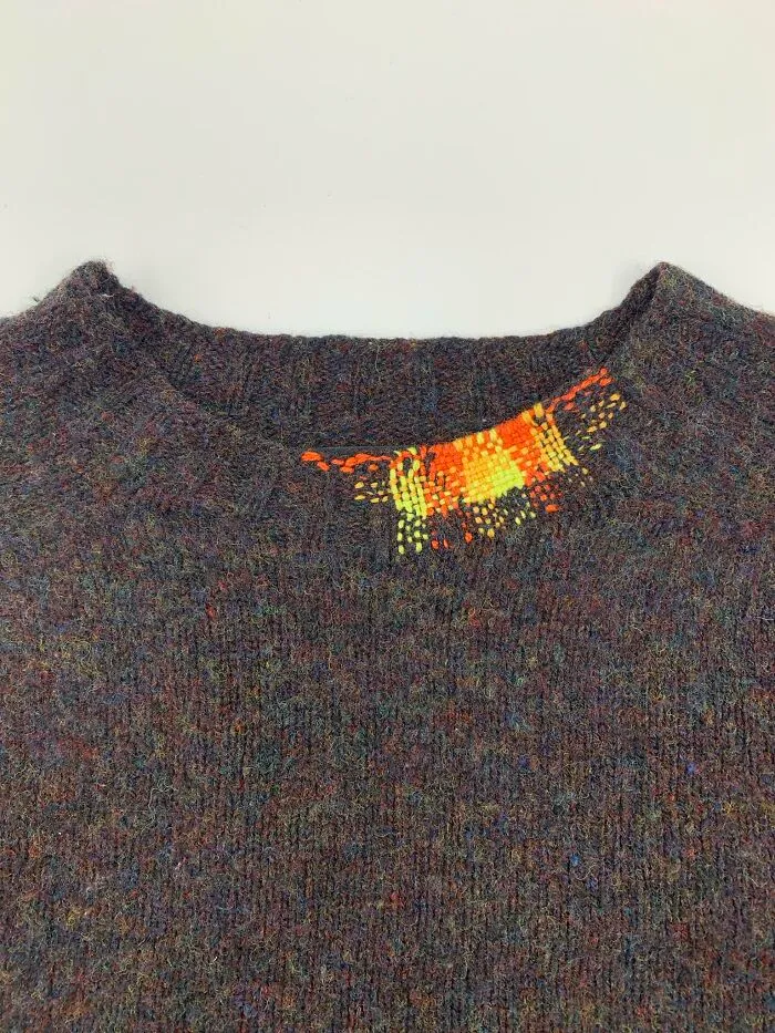 Colorful woven repair on a dark sweater collar showing how a little creativity saves money