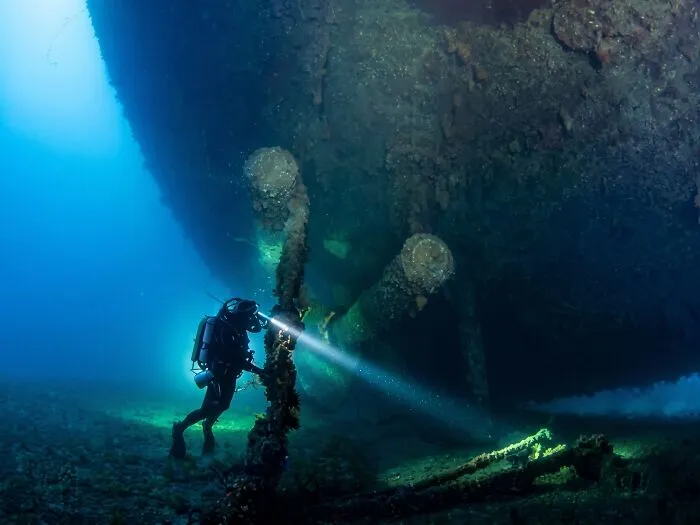 Diver examining submerged objects near the propeller of a massive ship wreck