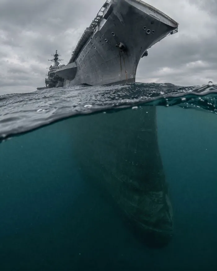 Split-level shot showing a massive warship hull extending deep underwater.