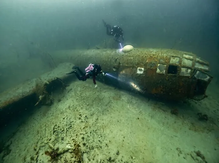 Scuba divers exploring submerged objects like an old rusty airplane wreck on the ocean floor.