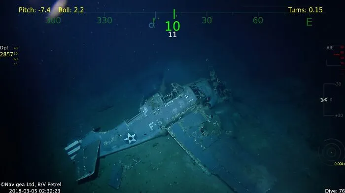 Sonar view of a sunken military airplane resting on the seabed among submerged objects underwater.