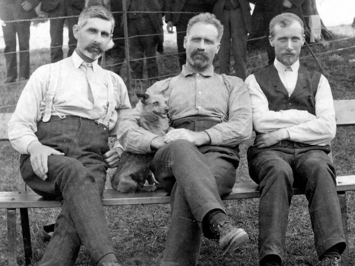 Vintage black and white photo of three men with a dog sitting together, representing historic cults