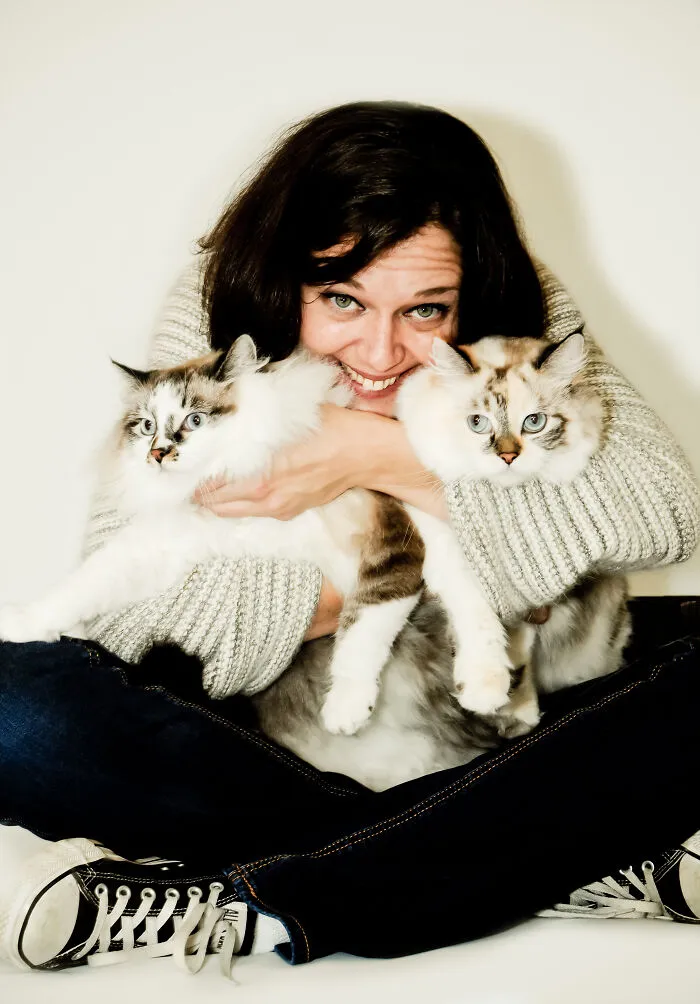 Smiling woman hugging two fluffy cats in a slightly awkward family photo