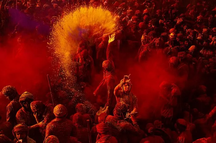 Large crowd covered in vibrant red and orange powder during festival photo awards