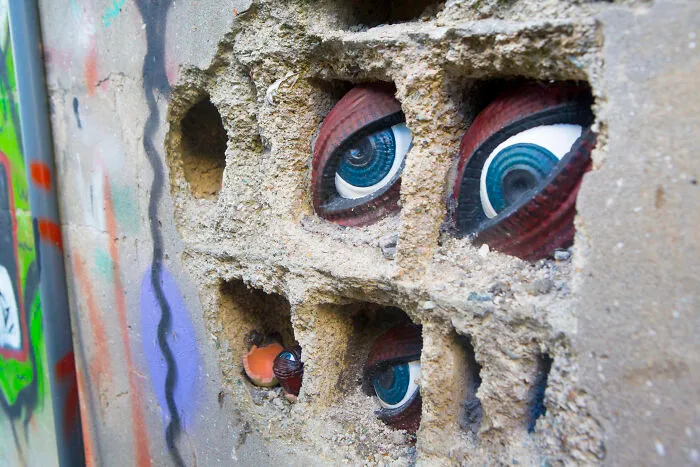 Spooky blue eyes peeking from brick wall crevices, a creative street art installation