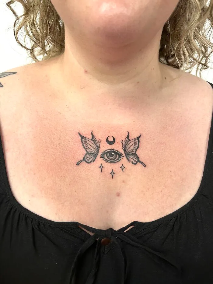 Black ink butterfly tattoo with an eye and crescent moon on upper chest