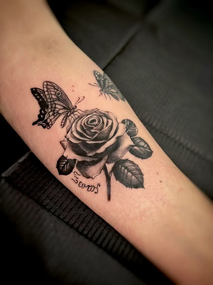 Realistic rose with two butterflies black tattoo on forearm