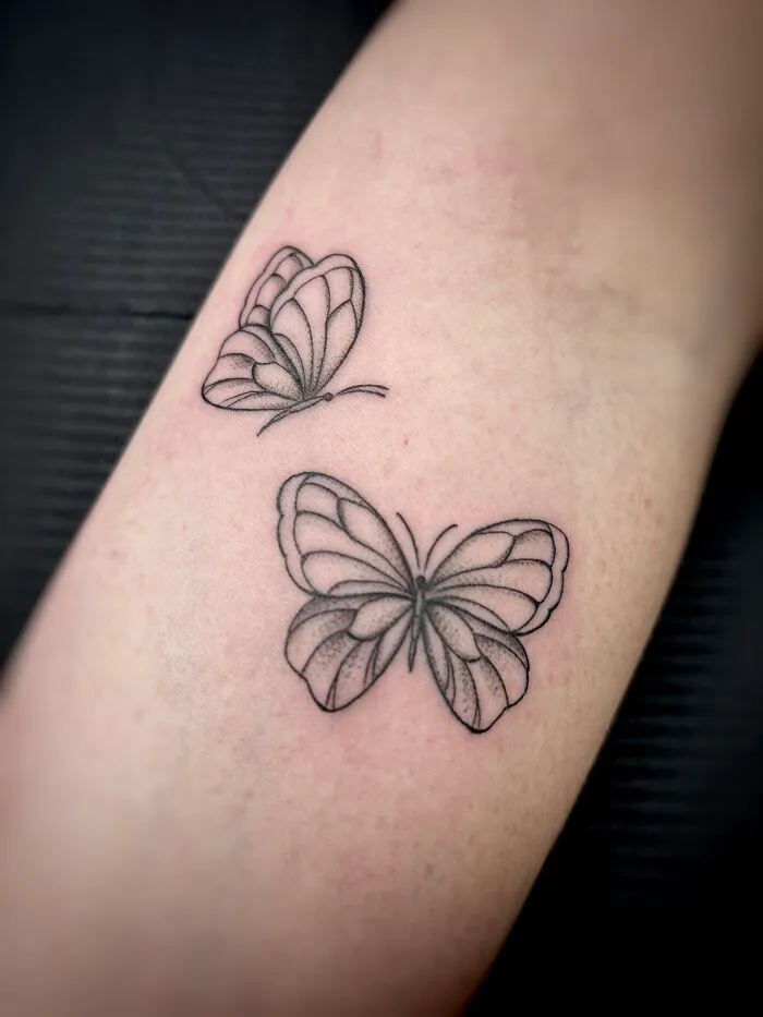 Minimalistic black outline butterfly tattoos on skin