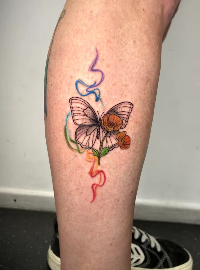 Transparent butterfly tattoo with colorful floral and smoke details on leg