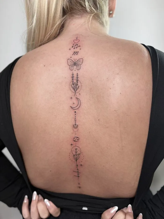 Delicate butterfly tattoo with moon and flowers along spine on back