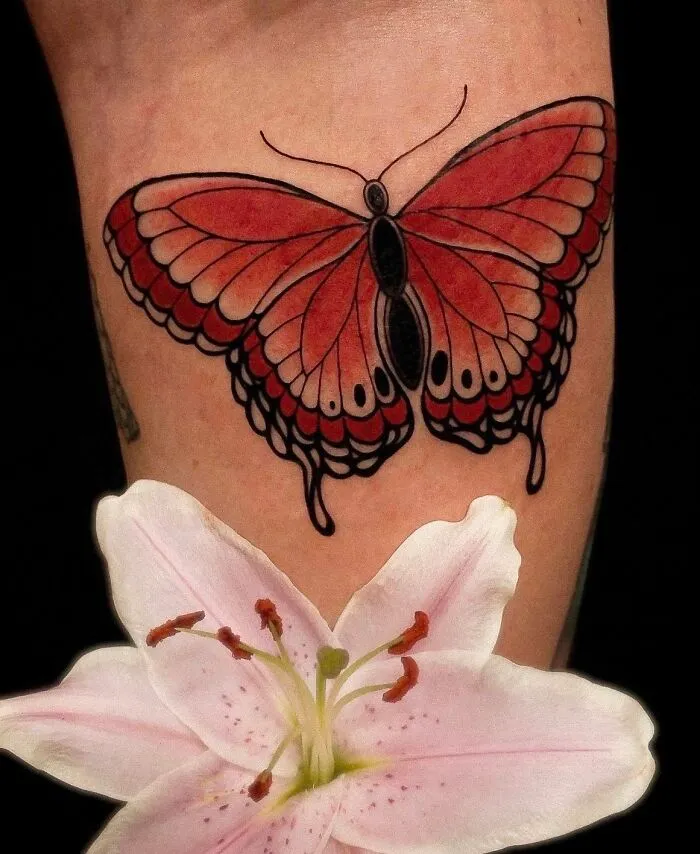 Red butterfly tattoo with detailed wings above pink flower