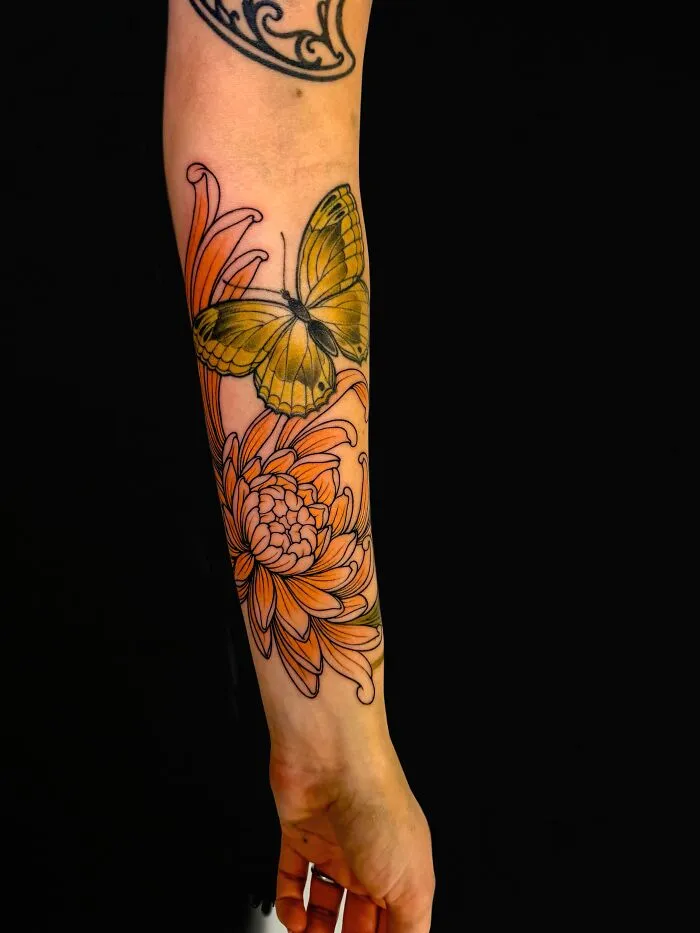 Yellow butterfly tattoo with orange flower on forearm