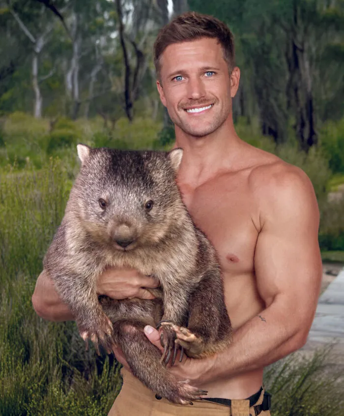 Shirtless Australian firefighter smiling while holding a large wombat