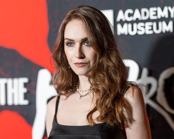 Trans actor with wavy brown hair posing on the red carpet at the Academy Museum in Hollywood