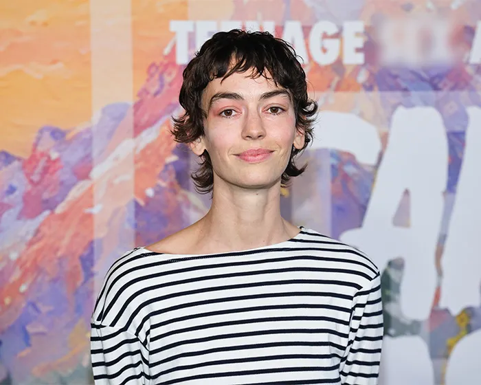Trans actor in a striped shirt posing against a colorful backdrop at a Hollywood event