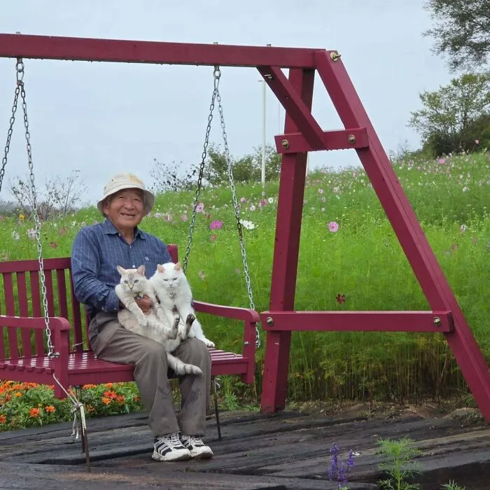 Japanese grandpa holding his two cute cats on a red swing set during a outdoor photoshoot.