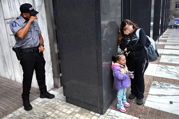 Security guard standing near distressed woman and child on city sidewalk, best pics 2026 Siena International Photo Awards