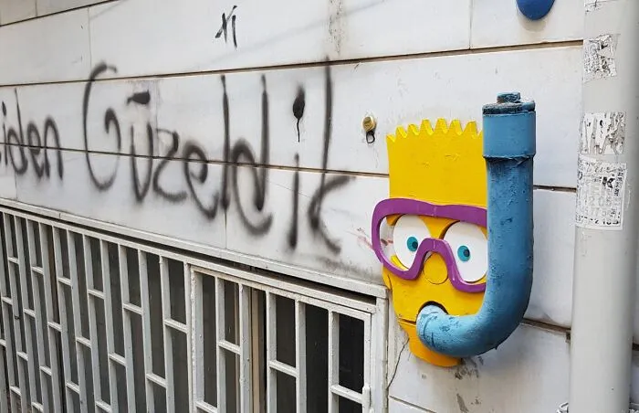 Creative art collective installation of Bart Simpson wearing a snorkel mask on a pipe along a city wall.