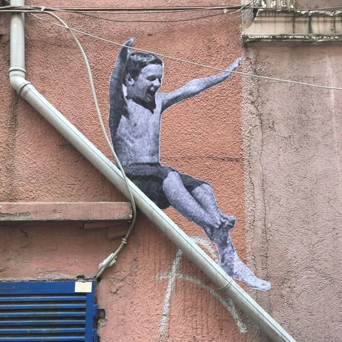 Creative art collective street art of a boy sliding down a pipe on a building wall