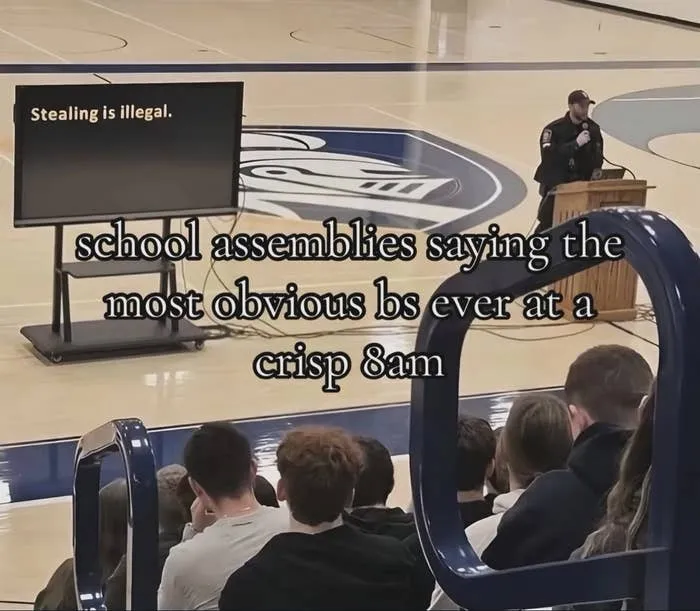 School assembly with a speaker and screen saying stealing is illegal in gymnasium
