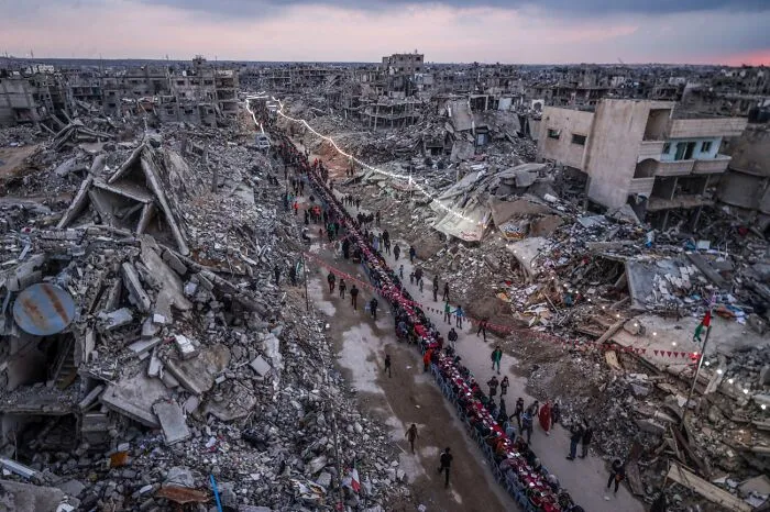 Long line of people walking through war-torn destroyed buildings showing urban devastation