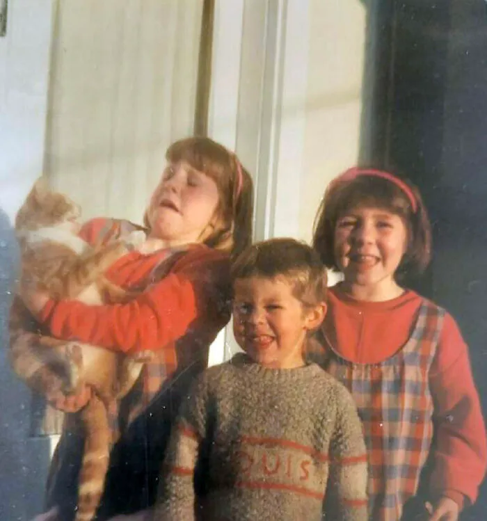 Three children posing with a cat that is struggling to escape, capturing awkward family photos with cats.