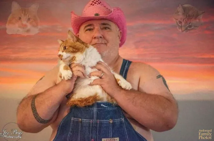 An awkward man in a pink cowboy hat holding his cat, a prime example of funny family photos with cats.